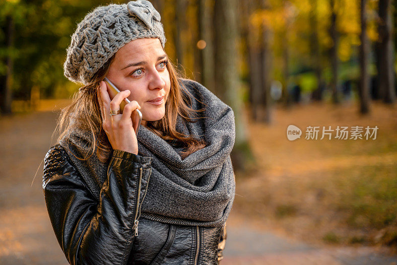 十几岁的女孩站在户外在美丽的秋天城市公园讲智能手机