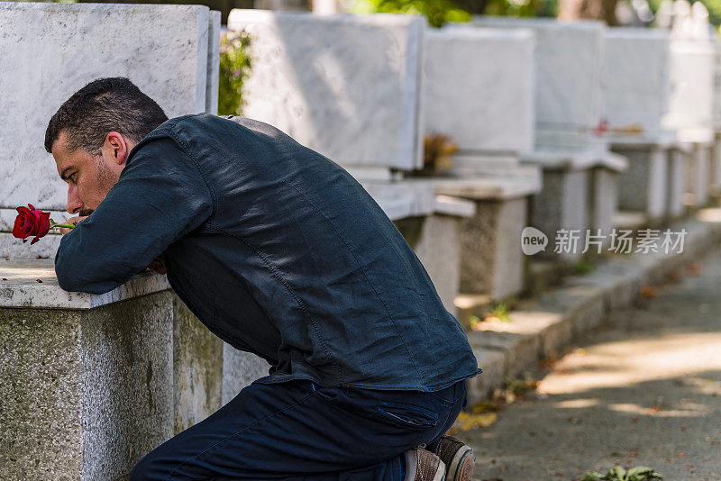 情绪紧张的黑衣男子跪在他已故朋友的墓前