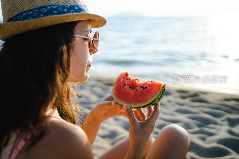 年轻女子在海滩上吃西瓜