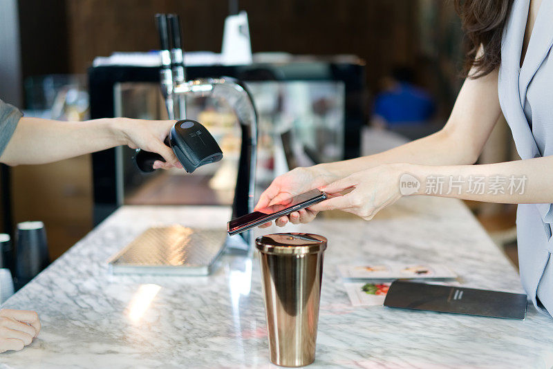 在餐厅柜台，女孩通过扫描二维码或智能手机上名为电子钱包的应用程序中的条形码来支付饮料。