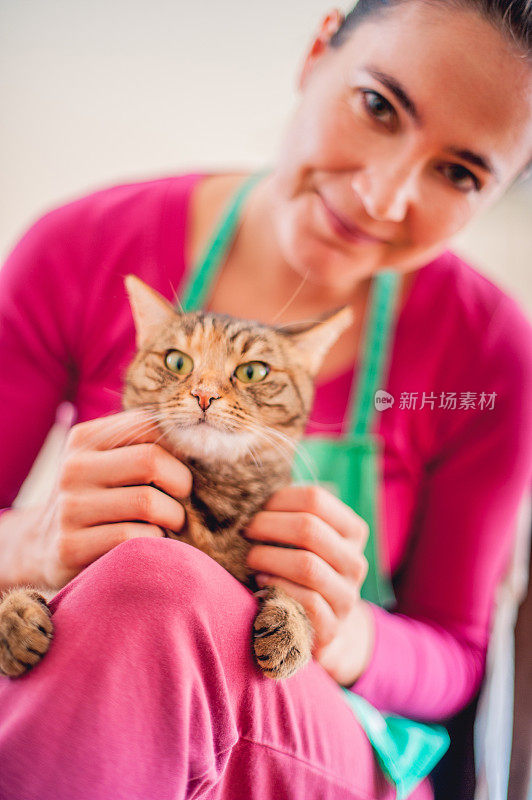 一名白人妇女在家里抚摸着猫，看着相机