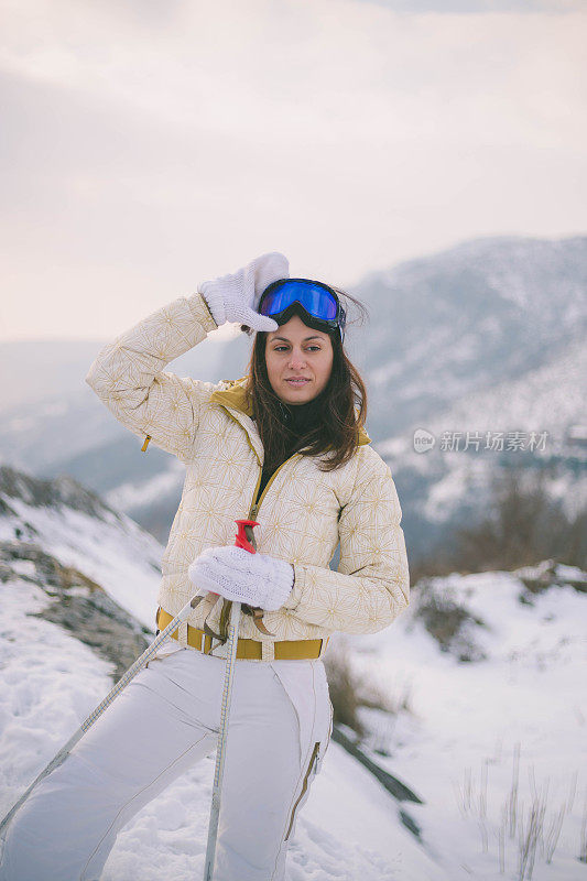 近景美丽的年轻女子在冬天的衣服站在一边，手拿木棍的背景雪山