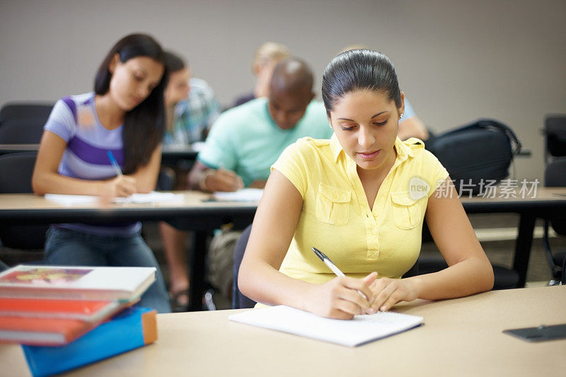 一个大学女生在学习，她的同学在模糊的背景中