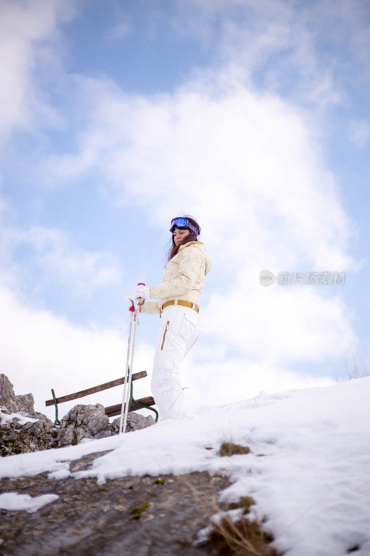 近景美丽的年轻女子在冬天的衣服站在一边，手拿木棍的背景雪山