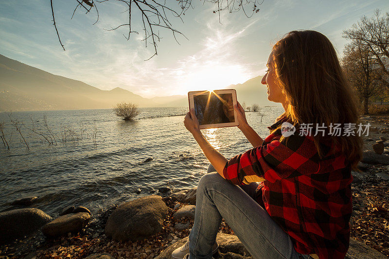 年轻女子坐在湖边，用着平板电脑