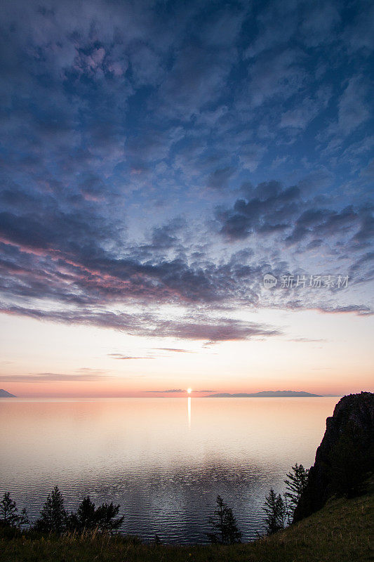 清晨的夕阳环绕着橙色和玫瑰色的岩石和奥尔孔岛和贝加尔湖的山脉