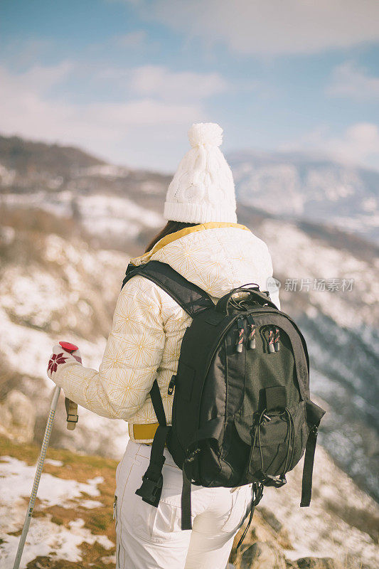 近景美丽的年轻女子在冬天的衣服站在一边，手拿木棍的背景雪山
