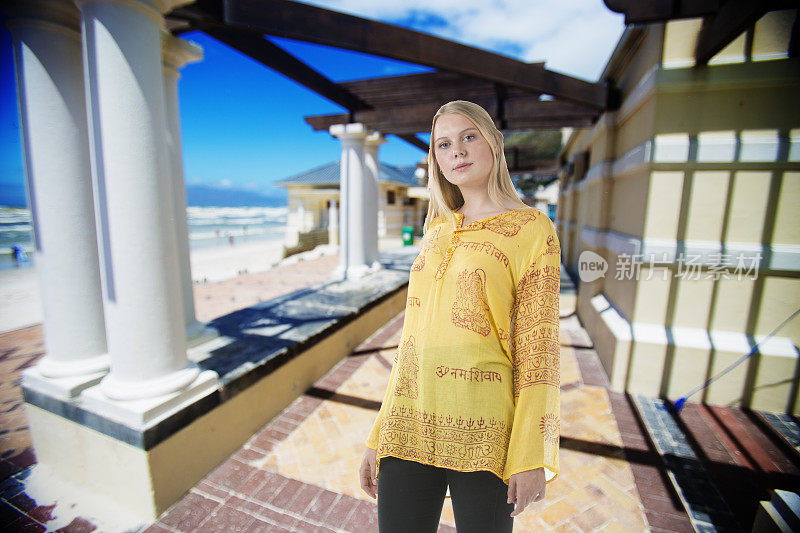 迷人的年轻女人与时尚的黄色上衣站在海滩附近的夏天
