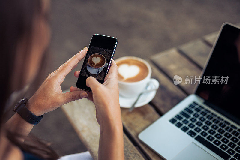 一个女人正在用智能手机拍一杯咖啡