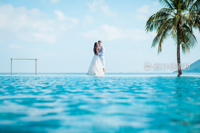 新婚夫妇在豪华度假村举行婚礼后。浪漫的新娘和新郎在游泳池附近放松。蜜月。