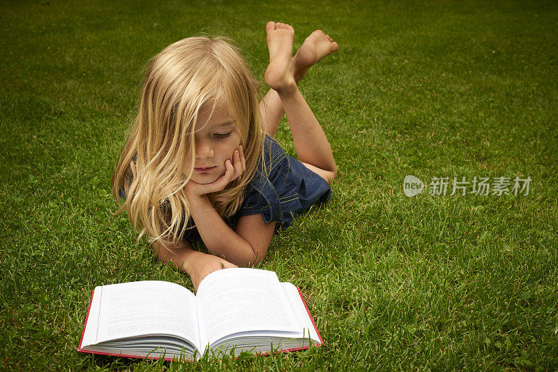 可爱的小女孩在草地上看书