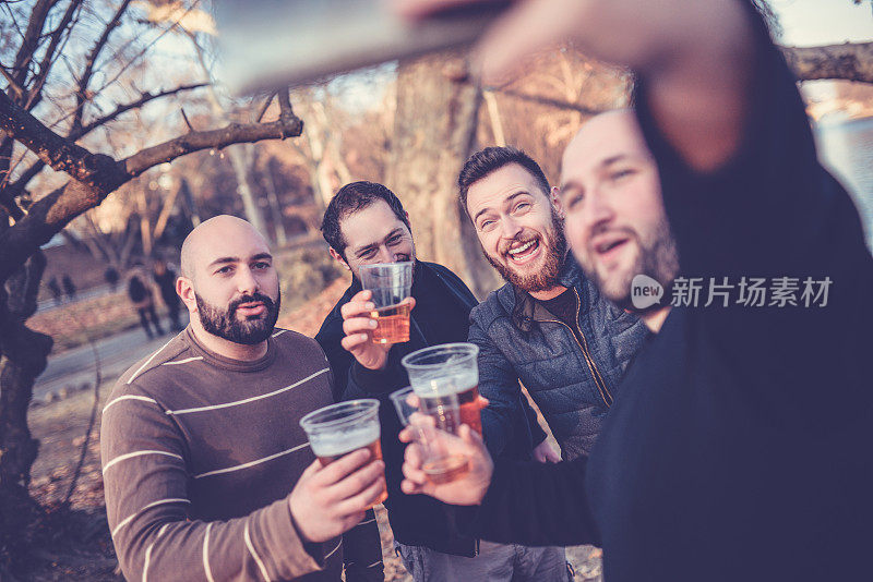一群微笑的朋友在公园里自拍，喝啤酒敬酒