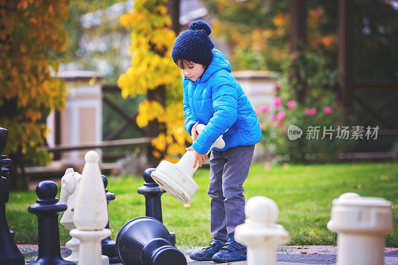 两个孩子，男孩兄弟，在公园里和巨大的人物下棋
