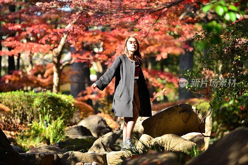年轻的日本女人走在踏石上穿过东京的小溪