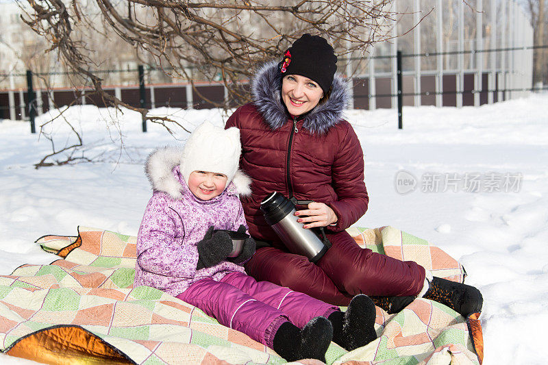妈妈和女儿在野餐时喝保温瓶里的茶。