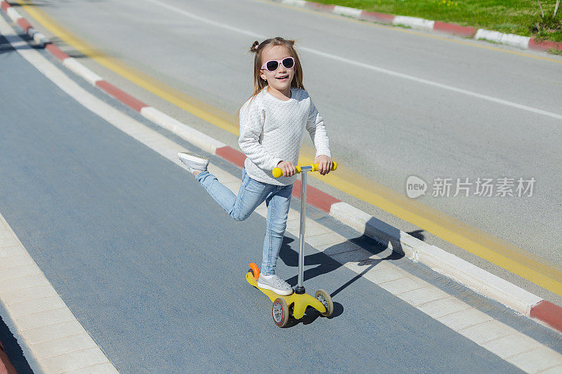 可爱快乐的女孩骑着推滑板车