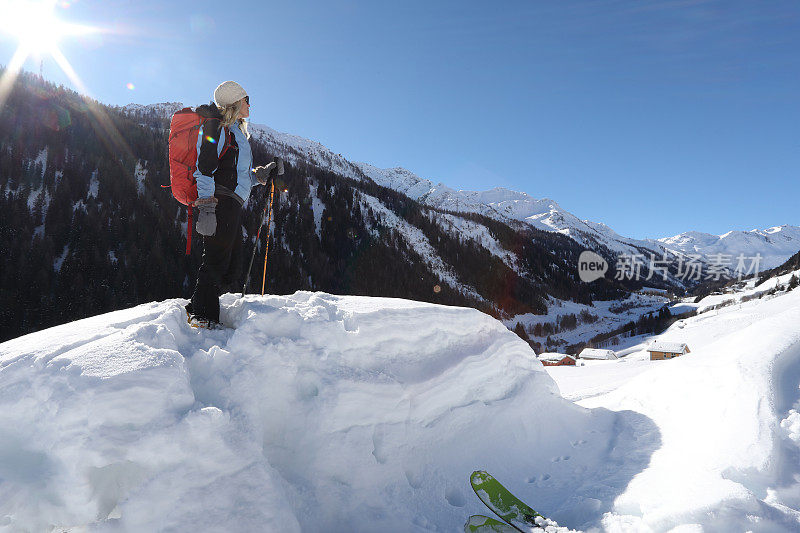女人扔下滑雪板，在厚厚的积雪中爬上山顶。