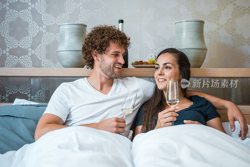 一对年轻夫妇躺在床上，喝着香槟庆祝搬家
