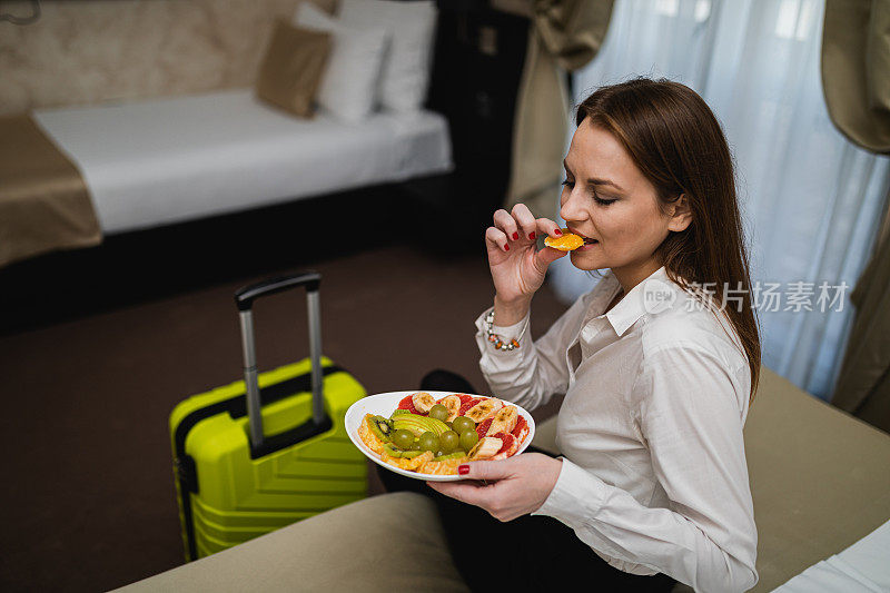 女商人拿着旅行箱在酒店房间吃水果