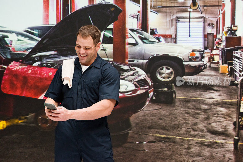 白人年轻男性体力工人在汽车修理店修理穿着工作服和使用手机
