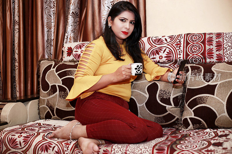 年轻的印度妇女舒舒服服地坐着喝茶