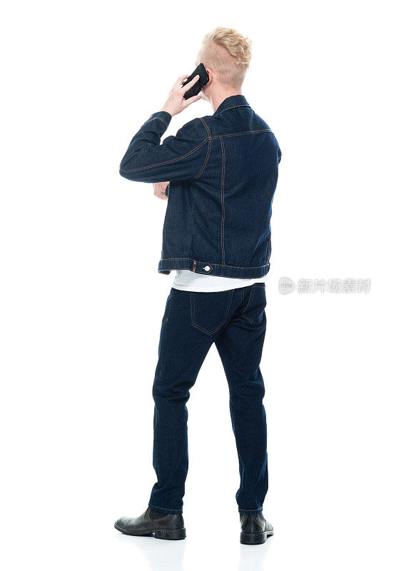 白人年轻男性穿着靴子站在白色背景前，拿着手机