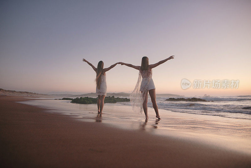 两名年轻女子在海边举起双手