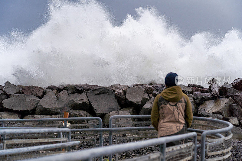 年轻人看着汹涌的海浪拍打在岩石码头上