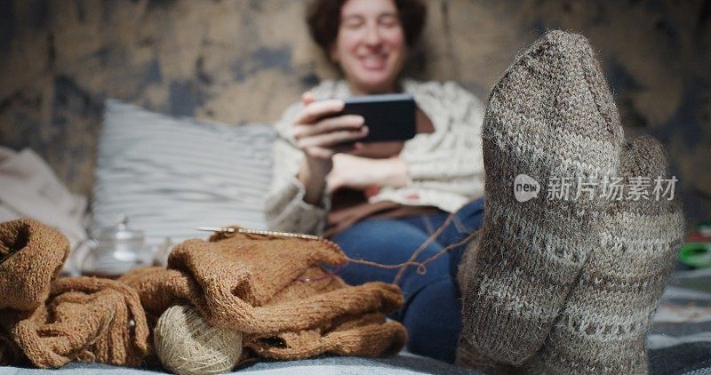 成熟的女人是坐在家里的沙发上一边打电话一边笑。注重脚上穿的羊毛手工袜子