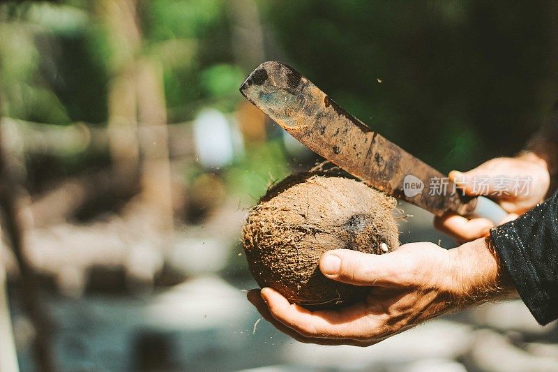 一个男人正在用大砍刀切开椰子