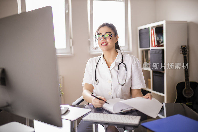 年轻女医生检查医疗文件和使用电脑在她的办公室