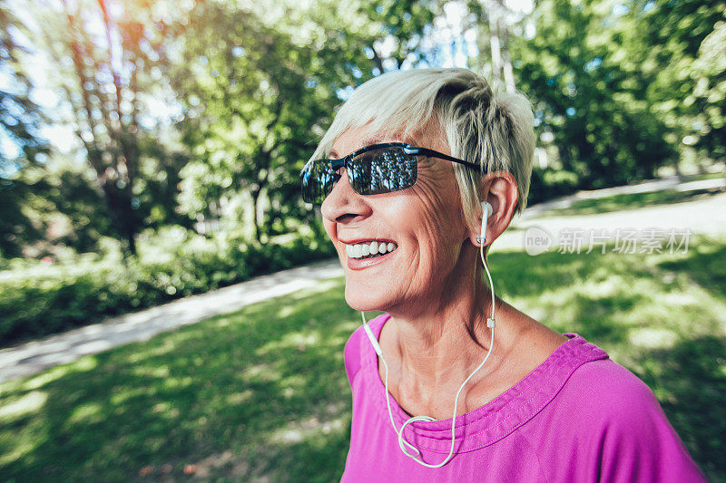戴着耳机在公园里跑步的老妇人