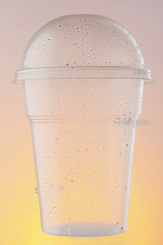 空塑料外卖杯，水杯。冰冷的一次性杯子，与水滴凝结在橙色的背景