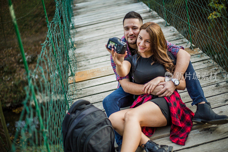 美丽的年轻登山夫妇，游客，呆在一起的自然。这对年轻夫妇正坐在连接峡谷两边的吊桥上，享受着美丽的时刻。