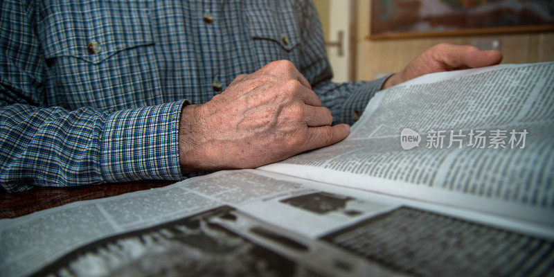 满脸皱纹的老人拿着报纸看新闻。