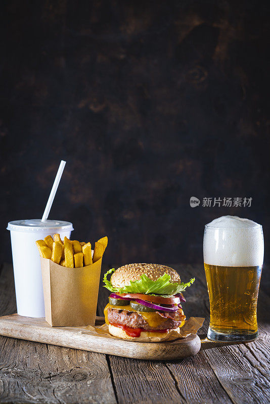 汉堡套餐，啤酒杯和一次性薯条在牛皮纸盒子在深色木桌上
