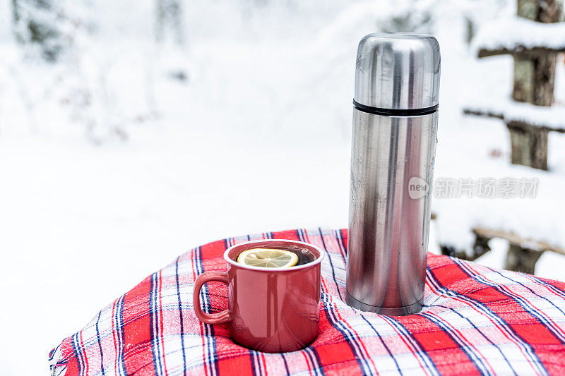 冬天的场景-大杯热饮和热水瓶在桌子上覆盖着格子。