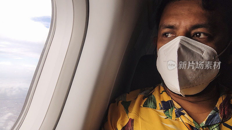 30多岁的拉丁裔男子，穿着黄色印花衬衫，戴着口罩，在飞机上看着窗外