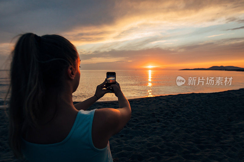 一名女子用手机拍摄美丽日落的背影。
