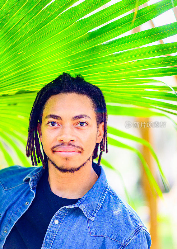 英俊的年轻黑人男子在热带树叶户外偷拍的头像，脸上露出可怕的笑容