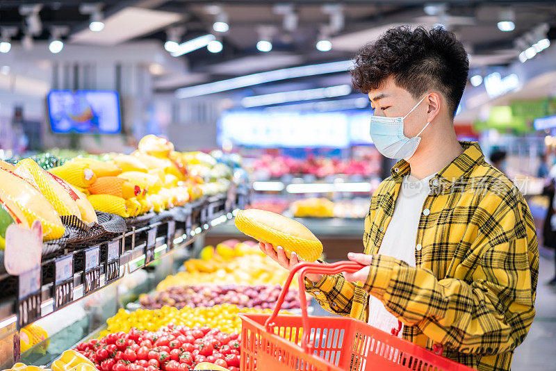 年轻英俊的亚洲男子戴着防护口罩，在超市买水果