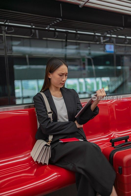 一名年轻的亚洲女商人的肖像照片旅行在通勤火车和红色行李在她的平板电脑上观看视频在旅程过境的商务旅行