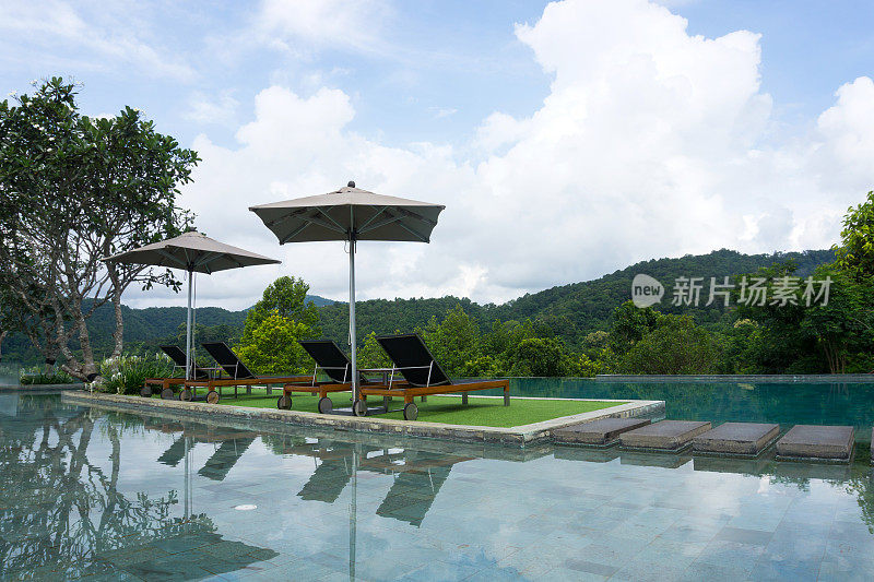 在泰国清迈，泳池旁边的甲板桌椅以山为背景