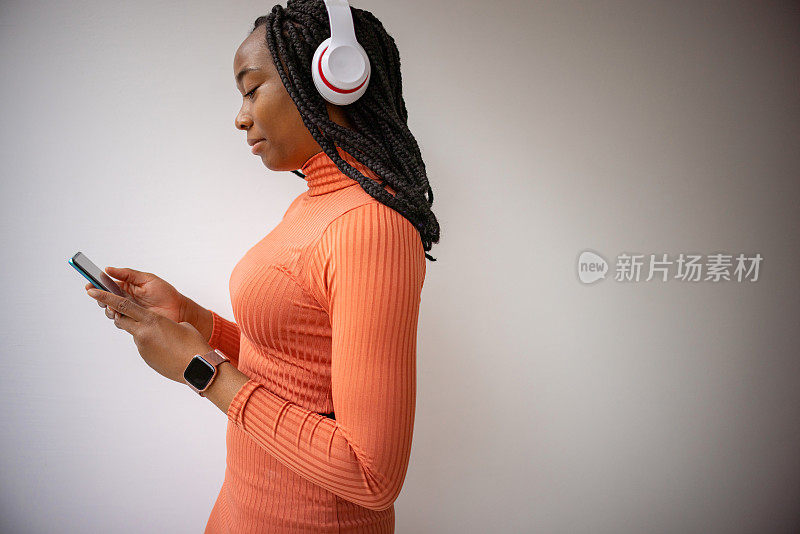 黑人妇女，戴着无线耳机，拿着手机，在她的播放列表中选择歌曲