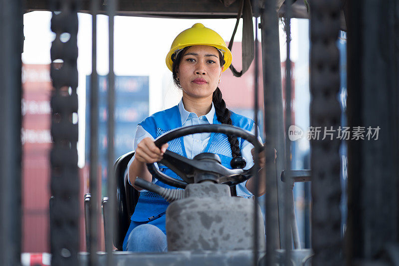 在货柜码头驾驶及操作货柜叉车的亚洲女性货柜堆场工人。女职工戴安全帽，穿制服，驾驶叉车在商业码头作业