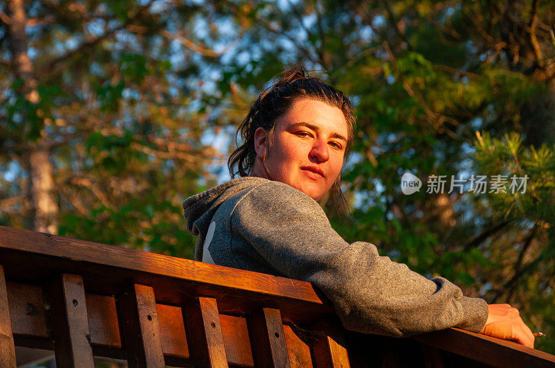 夕阳西下时，一名妇女望着以树木为背景的木栏杆