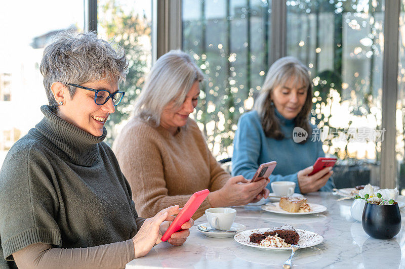 三位女性长辈朋友使用智能手机和社交网络，成熟女性科技生活方式，自助餐厅和早餐时刻