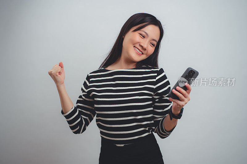 拿着智能手机的亚洲女子高兴地兴奋地在游戏中获胜，孤立在白色背景上。