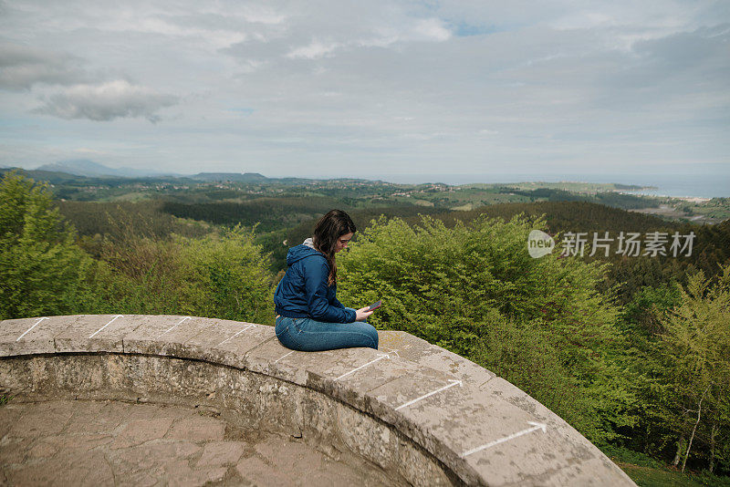 一个女人坐在观景台上看她的智能手机