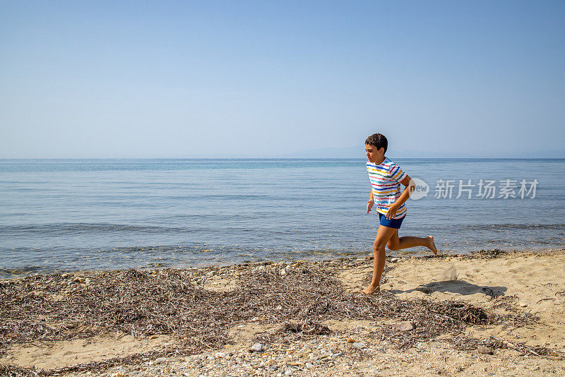 在阳光明媚的早晨，穿着衬衫和泳衣的男孩在海滩上奔跑